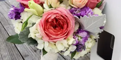 A wedding bouquet with pink and white roses, purple stock, and white hydrangeas resting on a wooden dock.