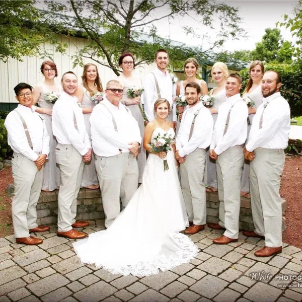 A wedding party including the bride, groom, and wedding party posing outdoors in front of a venue building.