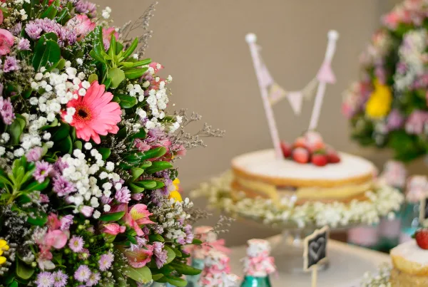 A close-up of a colorful flower arrangement with pink gerberas and white filler flowers next to a small cake.