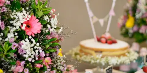 A close-up of a colorful flower arrangement with pink gerberas and white filler flowers next to a small cake.