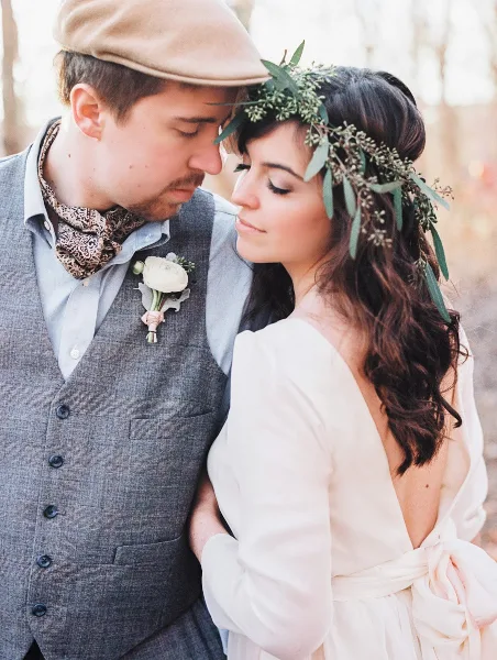A bride with styled hair and a floral crown posing with a groom in a wedding portrait.