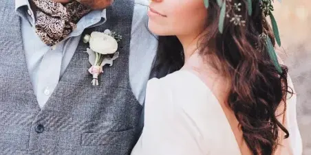 A bride with styled hair and a floral crown posing with a groom in a wedding portrait.