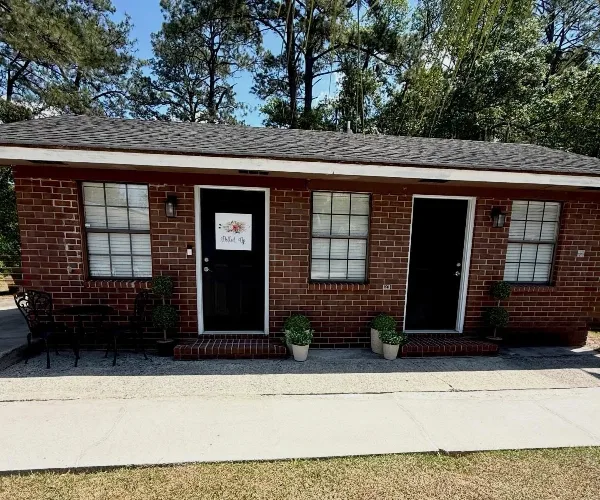 Exterior view of a brick studio building with a 'Dolled Up' sign on the front door.