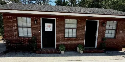 Exterior view of a brick studio building with a 'Dolled Up' sign on the front door.