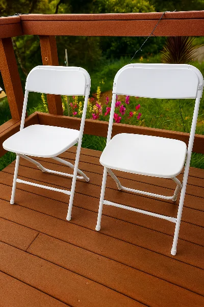 Two white folding chairs placed on a wooden deck with a garden background.