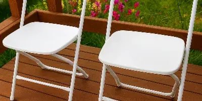 Two white folding chairs placed on a wooden deck with a garden background.