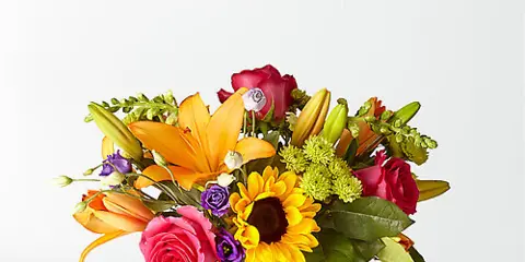 A vibrant floral arrangement featuring orange lilies, pink roses, and a sunflower in a clear glass vase.