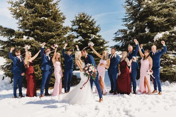 A wedding party posing in a snowy landscape with evergreen trees