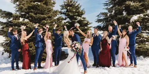 A wedding party posing in a snowy landscape with evergreen trees