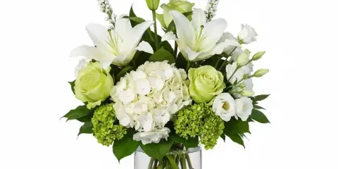 A floral arrangement with white lilies, green roses, and white hydrangeas in a clear glass vase.