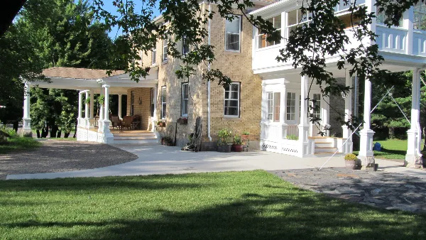 Exterior view of the Oldenburg House, a historic brick building with white porches and a grassy lawn.