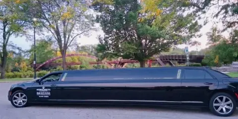 A black stretch limousine with Mid Michigan Limo branding parked on a street near a park.
