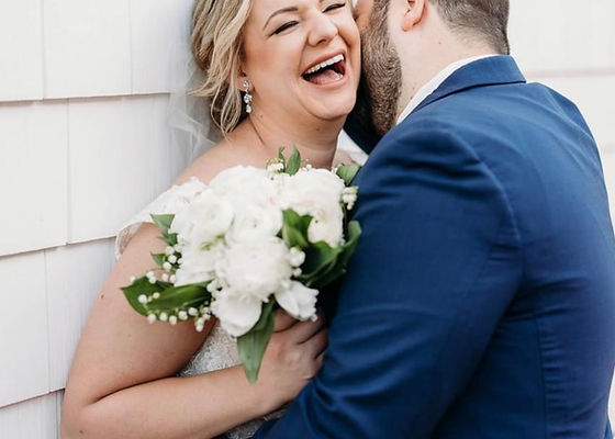 A bride holding a white floral bouquet while embracing a groom in a blue suit.