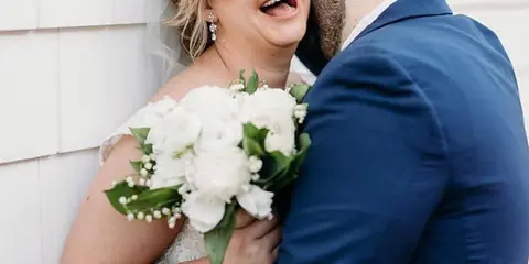 A bride holding a white floral bouquet while embracing a groom in a blue suit.