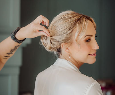 A professional stylist styling a bride's hair into an updo.