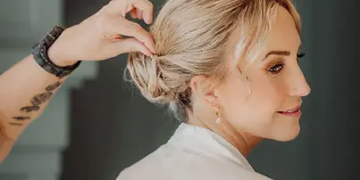 A professional stylist styling a bride's hair into an updo.