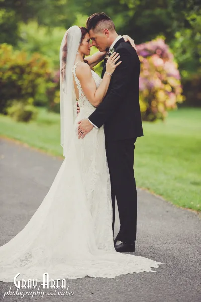 A bride and groom embracing in a garden setting, wearing formal wedding attire.
