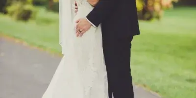A bride and groom embracing in a garden setting, wearing formal wedding attire.
