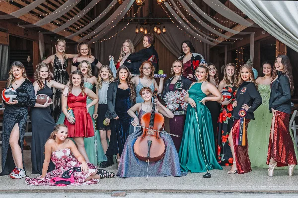 A group of high school seniors posing for a formal portrait in a rustic venue, holding sports equipment and a cello.