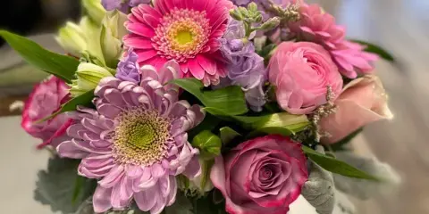 A fresh bouquet of pink and purple flowers, including roses, chrysanthemums, and lilies, arranged in a glass vase.
