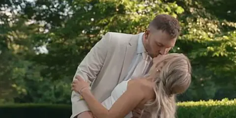 A bride and groom sharing a kiss in an outdoor garden setting.