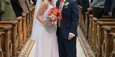 A bride and groom kissing in the aisle of a church during their wedding ceremony, surrounded by guests.