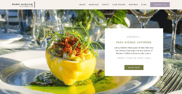 A plated gourmet dish with green garnish and sauce on a white plate at a formally set table with glassware.