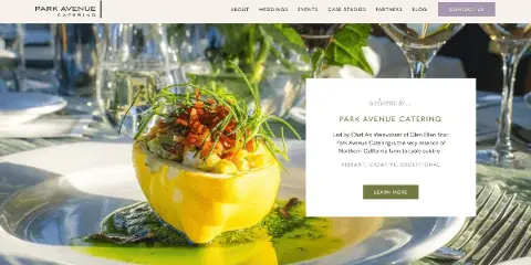 A plated gourmet dish with green garnish and sauce on a white plate at a formally set table with glassware.