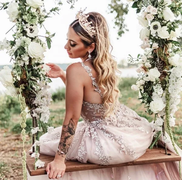 A bride with styled hair and makeup sitting in a floral arch.