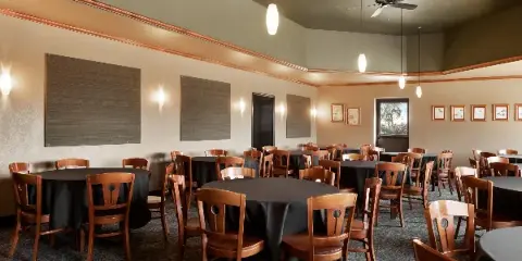 Interior of an event hall with round tables and wooden chairs set up for a gathering.