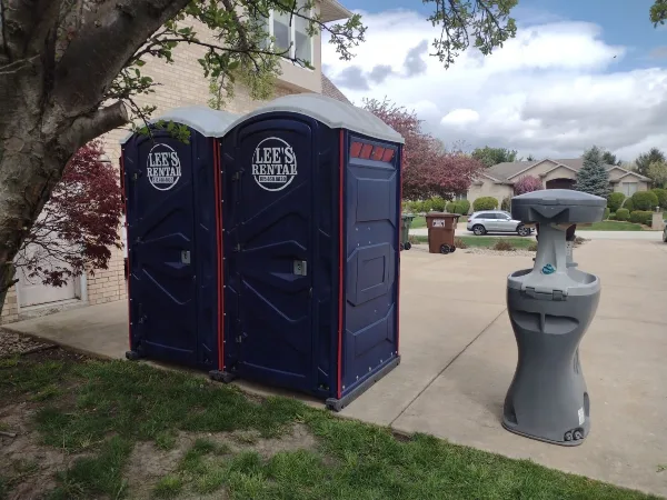 Two blue portable toilets and a gray hand-washing station with Lee's Rental logos set up on a driveway.