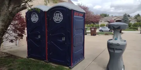 Two blue portable toilets and a gray hand-washing station with Lee's Rental logos set up on a driveway.