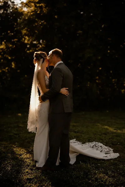 A bride and groom embracing in a romantic, moody outdoor portrait with dramatic lighting.