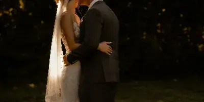 A bride and groom embracing in a romantic, moody outdoor portrait with dramatic lighting.