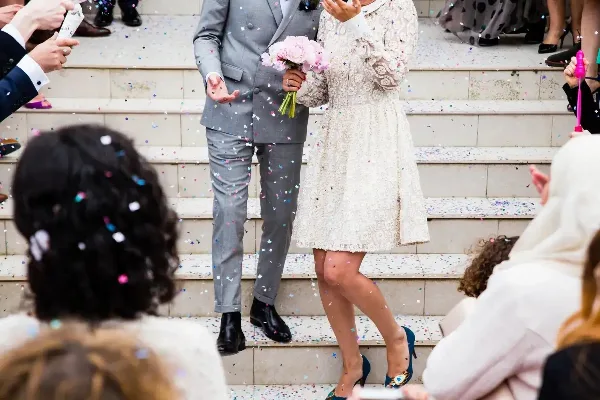 Wedding couple on steps surrounded by guests and falling confetti during a celebration.