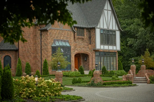 Exterior view of a large brick and timber-framed estate with a stone driveway and manicured landscaping.