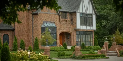 Exterior view of a large brick and timber-framed estate with a stone driveway and manicured landscaping.