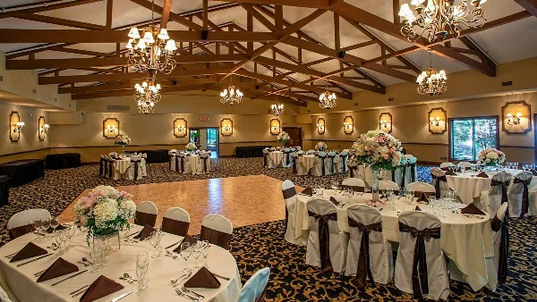 Wedding banquet hall with round tables, floral arrangements, and a central dance floor under a timber-beamed ceiling.