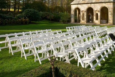 Rows of white folding chairs arranged on a lawn for an outdoor event.