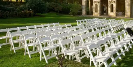 Rows of white folding chairs arranged on a lawn for an outdoor event.