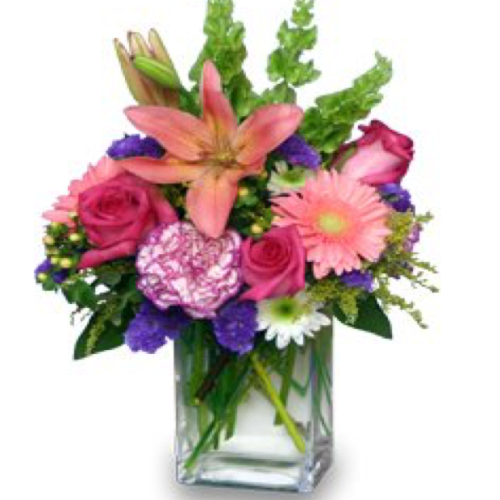 A vibrant floral arrangement featuring pink lilies, roses, and carnations in a clear glass vase.