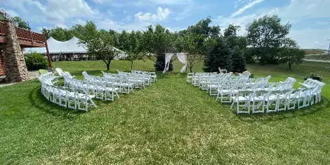 Outdoor wedding ceremony setup with rows of white chairs, a floral arch, and a white tent in the background.