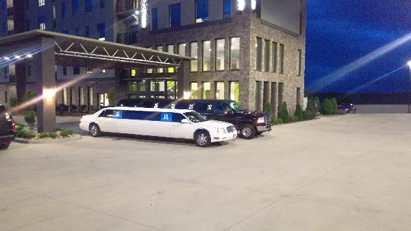 A white stretch limousine and a black SUV parked in front of a hotel entrance at night.