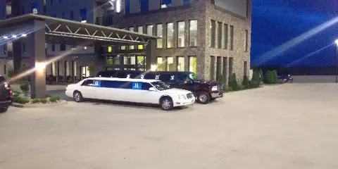 A white stretch limousine and a black SUV parked in front of a hotel entrance at night.