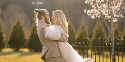 A bride and groom embracing in a grassy field with a blooming tree in the background.