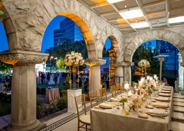 A wedding reception set up under the stone arches of Rhodes Hall, featuring a long table with floral centerpieces and guests in the background.