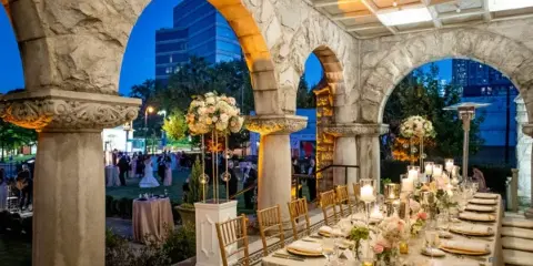 A wedding reception set up under the stone arches of Rhodes Hall, featuring a long table with floral centerpieces and guests in the background.
