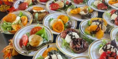 A long table filled with numerous plates of bruschetta appetizers, garnished with balsamic glaze and fresh vegetables.