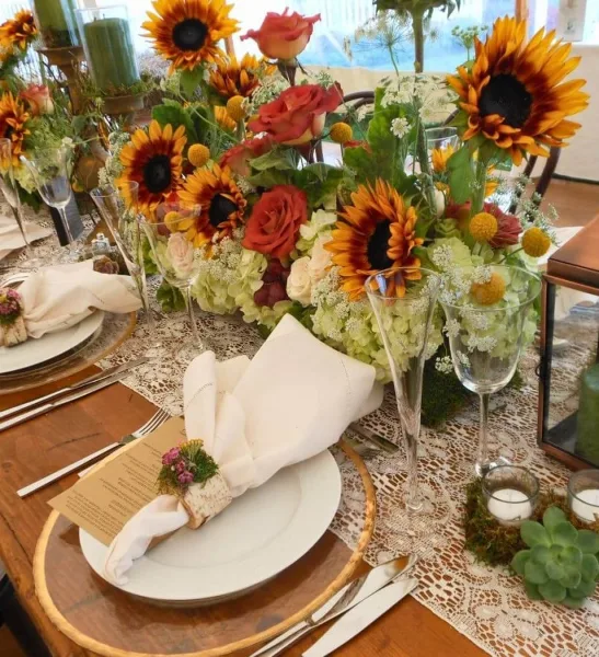 Elegant event table setting with sunflower and rose centerpieces, white napkins, glassware, and place settings.