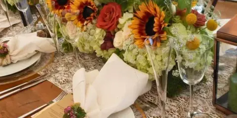 Elegant event table setting with sunflower and rose centerpieces, white napkins, glassware, and place settings.